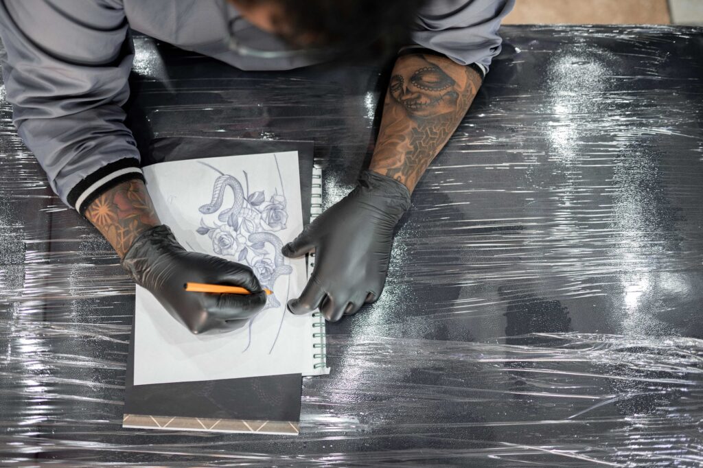 A tattoo artist is drawing a design stencil on his work stretcher before tattooing